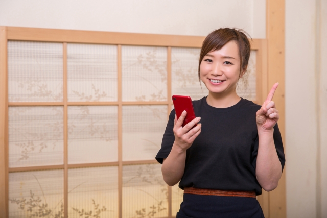 居酒屋でスマホを片手に人差し指をたてる女性