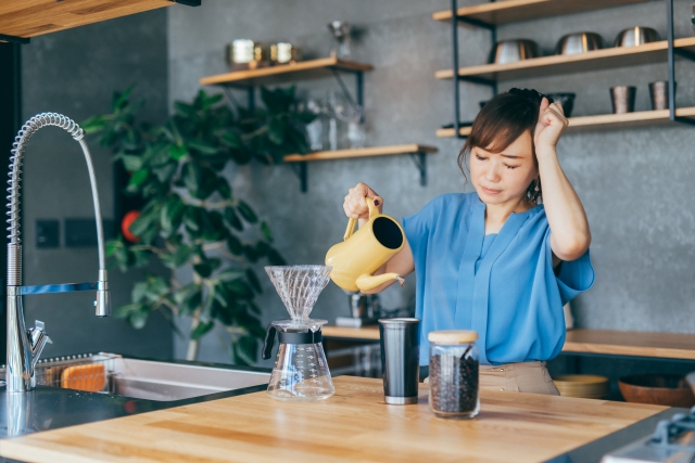 頭を抱えてコーヒーを淹れる女性